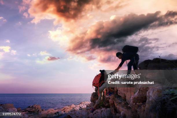 asian men stretches his hand to help lift his friend up  the hill . teamwork , helps ,climbing concept. - young man asian silhouette stock pictures, royalty-free photos & images