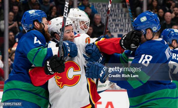 Dillon Dube of the Calgary Flames gets a hand in the face of Jake Virtanen of the Vancouver Canucks while held by Jordie Benn during NHL action at...