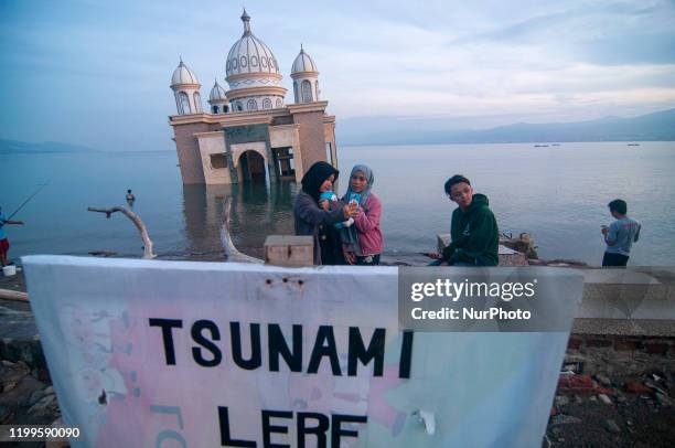 Residents take pictures against the background of the floating mosque that collapsed into the sea on the coast of Kampung Lere, Palu, Central...