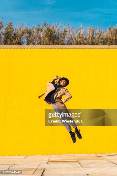 young man dancing in front of yellow wall, jumping mid air - fashion show foto e immagini stock