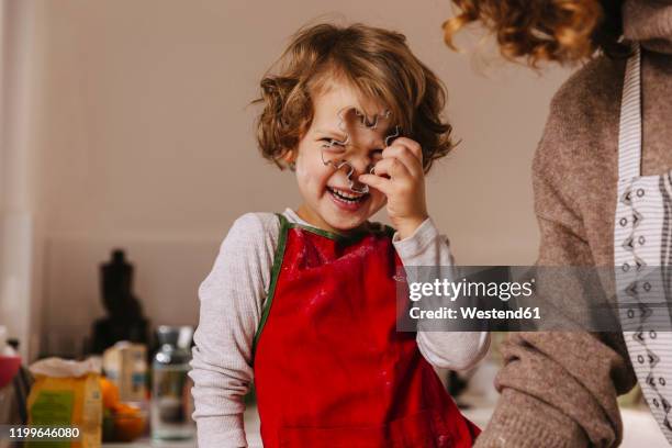 playful girl with her mother holding christmas cookie cutter in kitchen - we're back stock-fotos und bilder