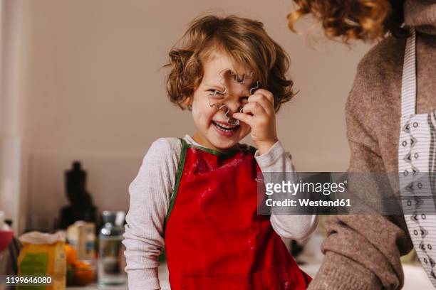 playful girl with her mother holding christmas cookie cutter in kitchen - heritage celebration inside stockfoto's en -beelden
