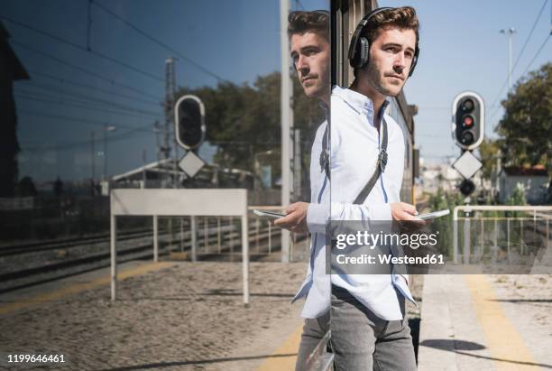young man with headphones and smartphone standing in train door - aussteigen stock-fotos und bilder