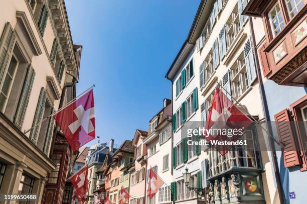 switzerland, canton of zurich, zurich, swiss flags hanging over historic augustinergasse lane - swiss flag stockfoto's en -beelden