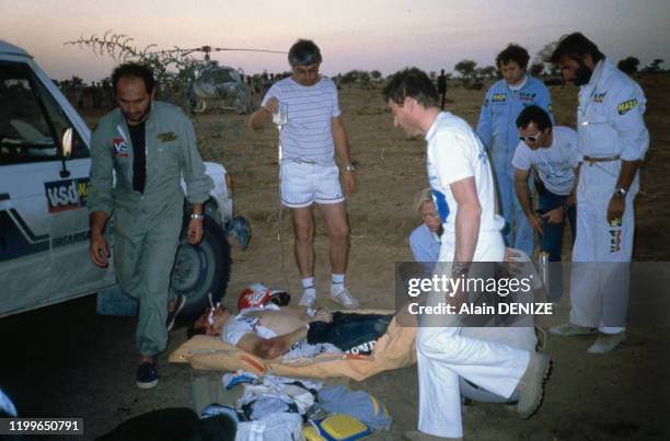 Equipe médicale et Thierry Sabine à droite auprès d'un blessé pendant le rallye automobile Paris-Dakar entre Agadez et Zinder le 9 janvier 1986,...