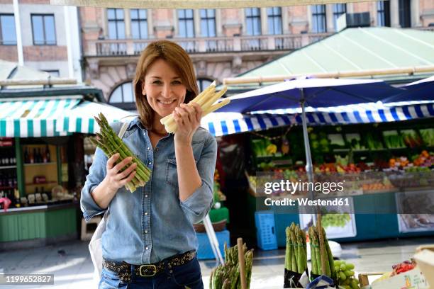 portrait of smiling mature woman choosing asparagus at a market stall - market stall stock-fotos und bilder