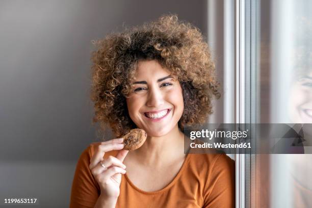 smiling mid adult woman eating a cookie - eating cookies foto e immagini stock