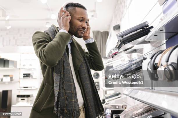 man trying headphones in a store - loja de produtos eletrônicos - fotografias e filmes do acervo
