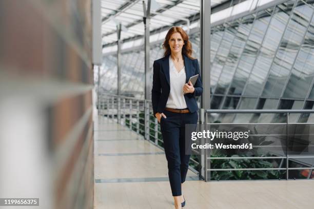 confident businesswoman holding a tablet in a modern office building - pant suit stockfoto's en -beelden