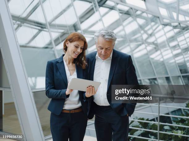 smiling businessman and businesswoman using tablet in modern office building - tablet 2 personen beratung stock-fotos und bilder