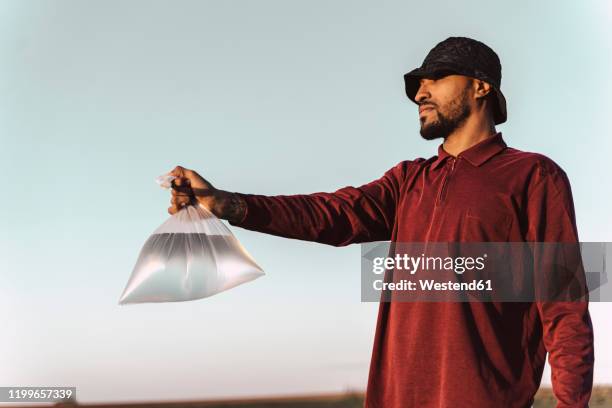young man holding plastic bag filled with water under blue sky - wassermangel stock-fotos und bilder