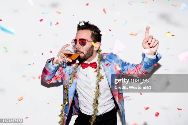 cool and stylish man wearing a colorful suit and sunglasses celebrating a party with confetti and drinking - sunglasses disguise imagens e fotografias de stock