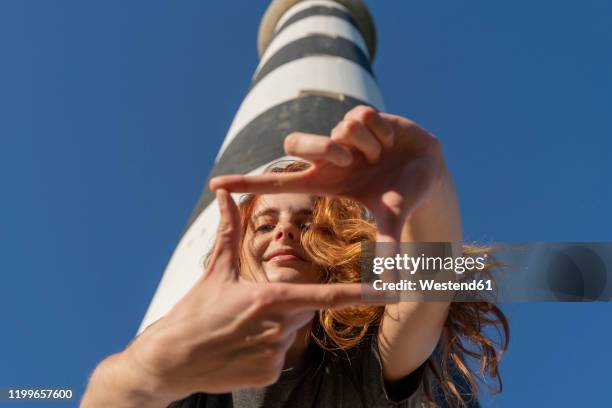 portrait of redheaded young woman at a lighthouse - finger frame stock-fotos und bilder