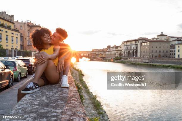 affectionate young tourist couple sitting on a wall at river arno at sunset, florence, italy - italy city break stock pictures, royalty-free photos & images