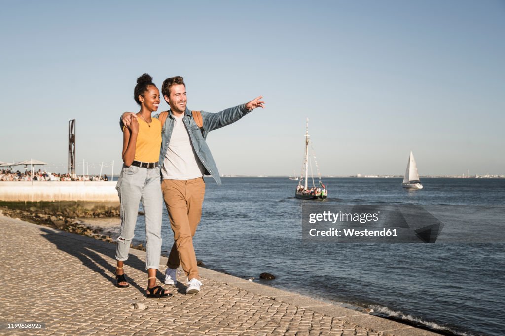 Happy young couple walking on pier at the waterfront, Lisbon, Portugal
