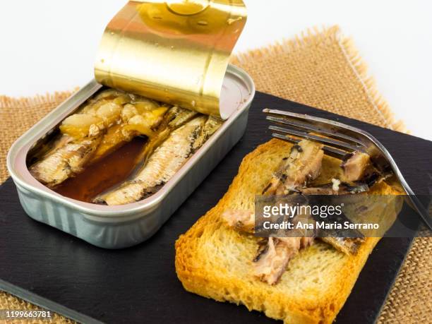 basic food: a can of sardines and a slice of toast on a slate plate and a fork on top of a burlap cloth - sardine can fotografías e imágenes de stock
