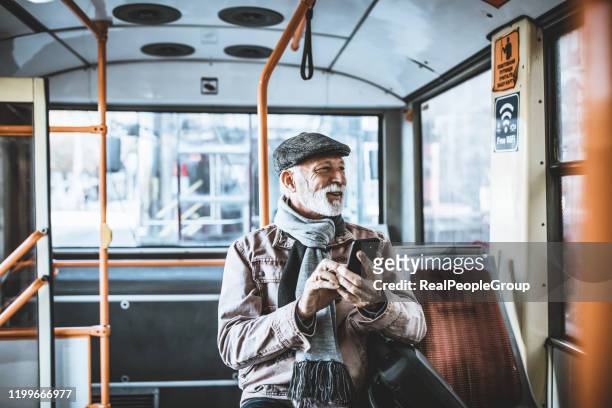 photo of mature businessman travelling by bus in city during winter day. senior male with beard traveling by bus and using his smart phone - man riding bus stock pictures, royalty-free photos & images
