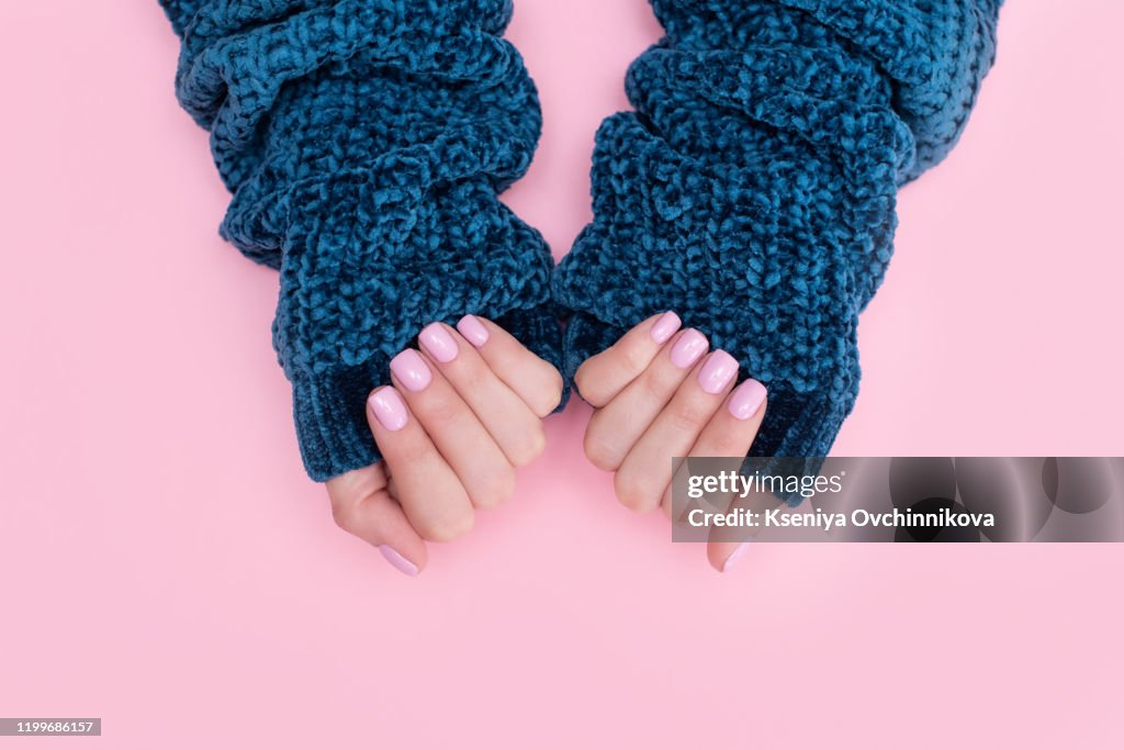 Female hands manicure close up view on pink knitted sweater background. Nail painting effects. Manicure salon banner concept