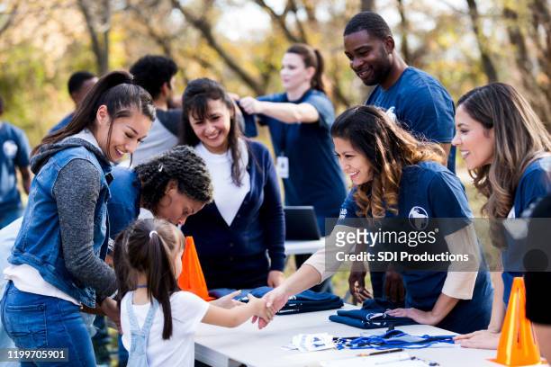 volontario adulto medio stringe la mano alla ragazza al tavolo di registrazione - community events foto e immagini stock