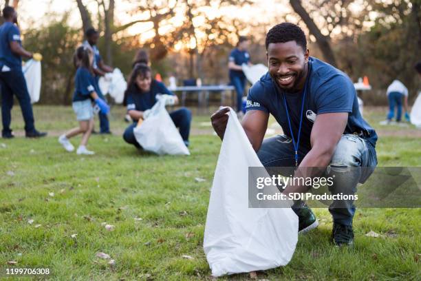 confident man picks up garbage in park - limpeza ambiental imagens e fotografias de stock