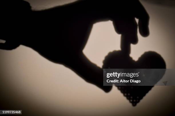 shadow on a wall of man's hand holding a heart: love. - german style icons stock pictures, royalty-free photos & images