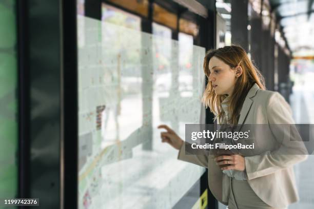 giovane imprenditrice adulta che guarda la mappa di una stazione degli autobus a buenos aires - bus shelter foto e immagini stock