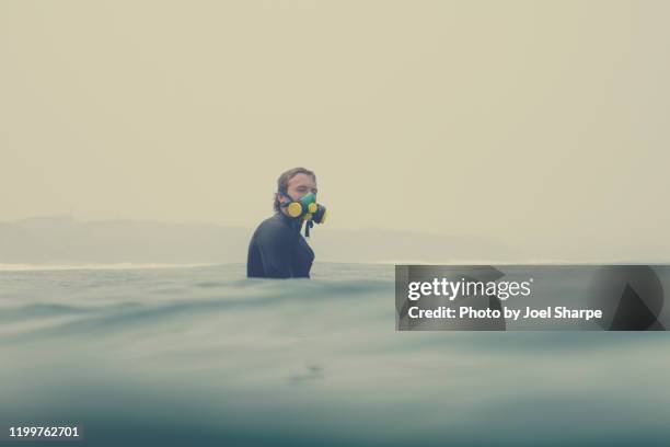 surfer at sea and wearing a respirator during a bushfire smoke haze - australia wildfires photos et images de collection