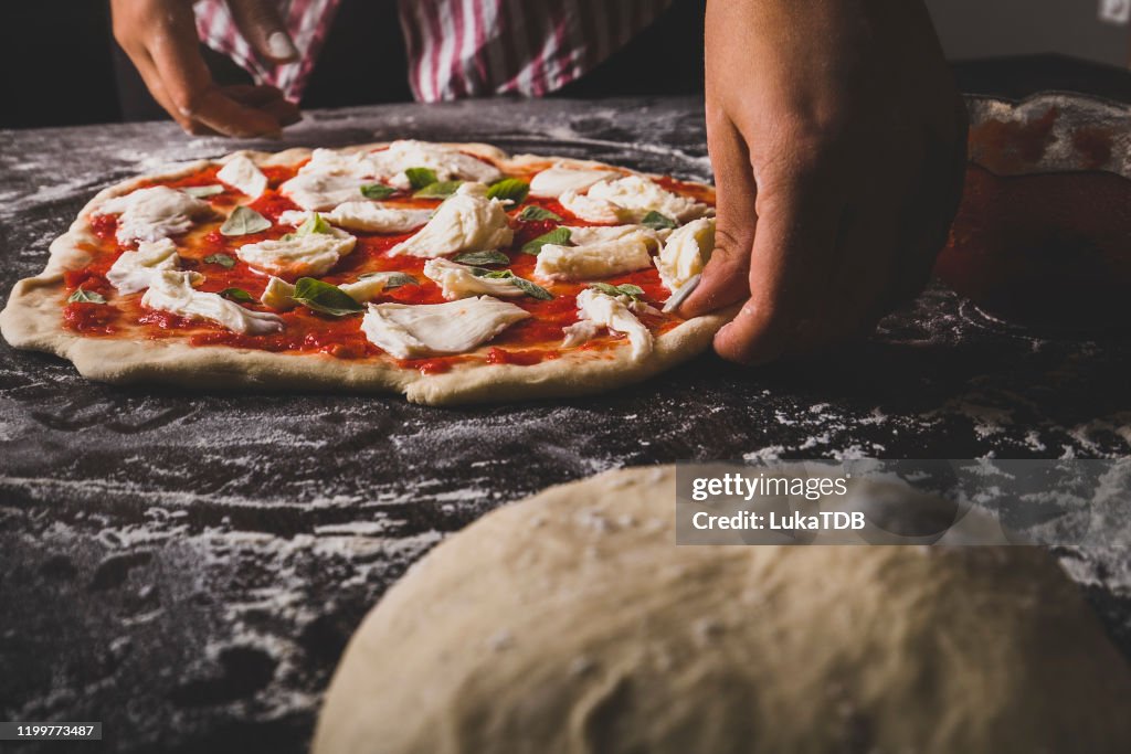 A chef preparing a cheese and basil pizza