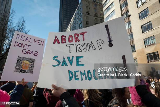 Marchers hold signs that say, "Abort Trump Save Democracy" and "Real Men Dont Grab" walking during the second annual Women's March in the borough of...