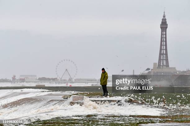 Man stands on the promenade as waves crash over the barriers in Blackpool, northern England, on February 10, 2020 as high winds brought by Storm...