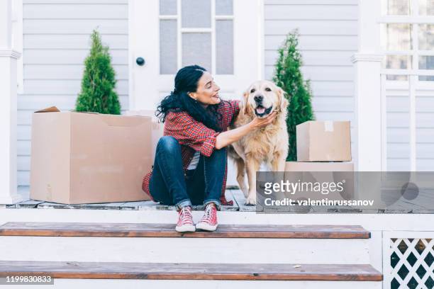 мid adult woman moving to new house and sitting on the stairs and petting her golden retriever - moving house stock pictures, royalty-free photos & images