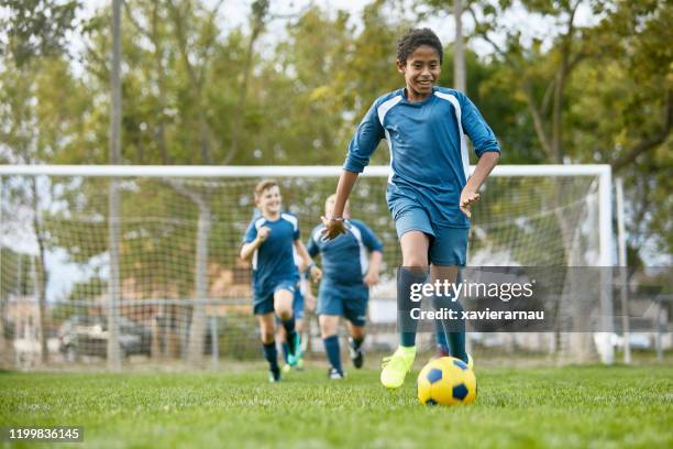 teenage mixed race footballer dribbling away from teammates - teenager playing football stock pictures, royalty-free photos & images