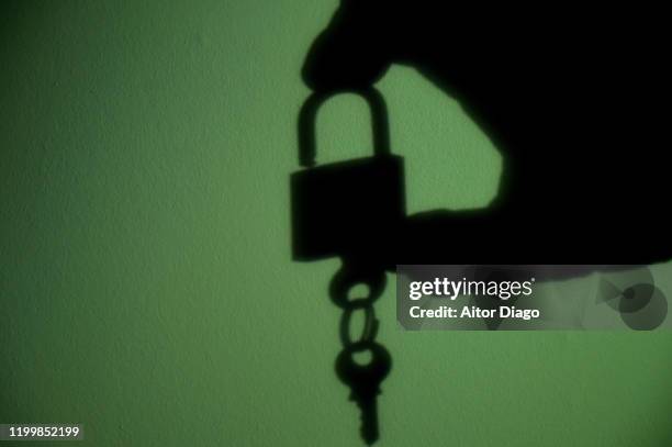 silhouette of a hand taking a key hanging of a padlock. green background. - open prison cell stock pictures, royalty-free photos & images