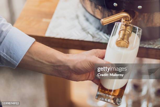 close-up of man pulling beer from a wooden barrel into a glass. - bavaria beer stock pictures, royalty-free photos & images