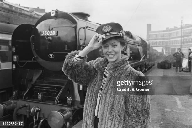 English actress Jenny Agutter wearing a railwayman's cap and posing in front of the Merchant Navy 4-6-2 class steam locomotive, 35028 Clan Line, 1st...