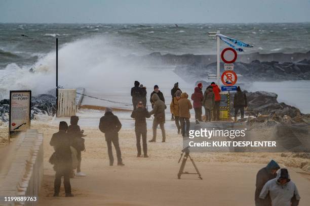 People stand on the beach as strong waves break against a jetty on the Belgian coast in Ostend on February 10 after storm Ciara swept over the...