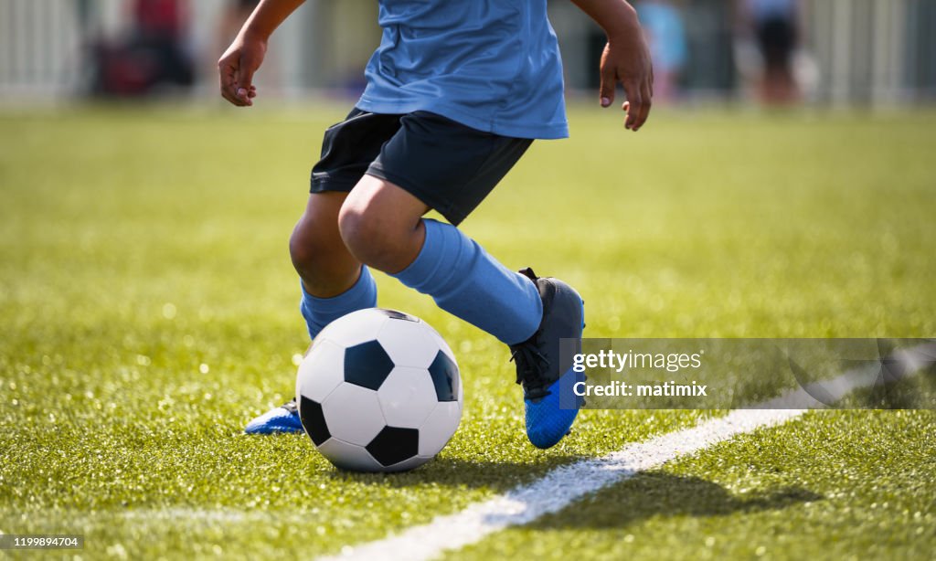 African American young boy playing soccer in a stadium pitch. Child running with soccer ball along the field white sideline. Junior soccer background