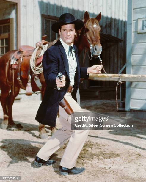 James Garner, US actor, poses in costume, pointing a handgun with a horse behind him, in a publicity portrait issued for the US television show,...