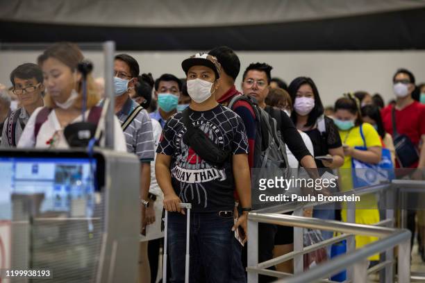 As Coronavirus spreads travelers arriving wait in line at immigration wear masks at Suvarnabhumi International airport in Bangkok, Thailand on...