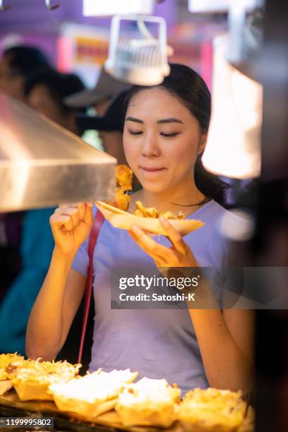 young woman eating takoyaki at night market - takoyaki stock pictures, royalty-free photos & images