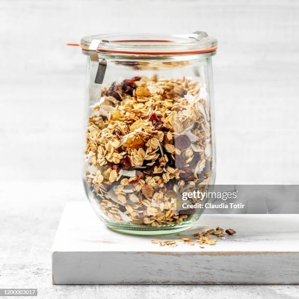 granola in a jar on a wooden cutting board on white background - knuspermüsli stock-fotos und bilder