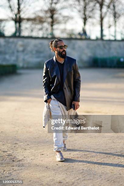 Jerry Lorenzo, Founder of "Fear of God" wears a black leather jacket, a t-shirt, white pants, shoes, sunglasses, outside Vuitton, during Paris...