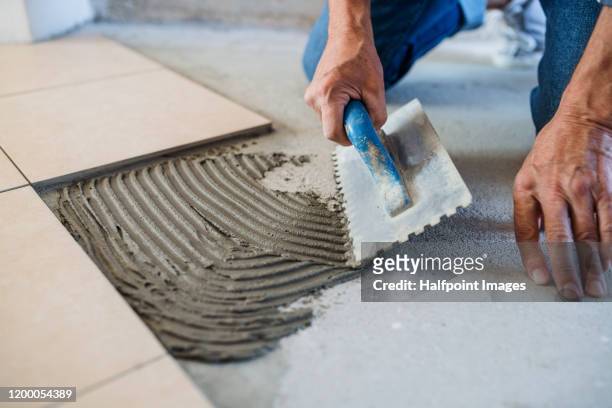 midsection of senior man laying tile floor in new home. - tegel stockfoto's en -beelden