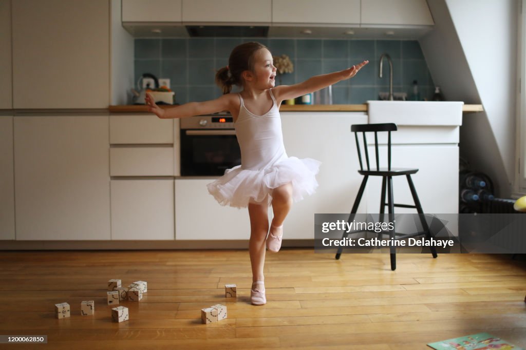 A 4 years old girl dressed as a dancer, dancing in the kitchen