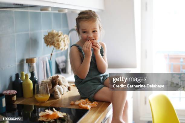 a 4 years old girl eating clementines in the kitchen. - 4 5 years foto e immagini stock