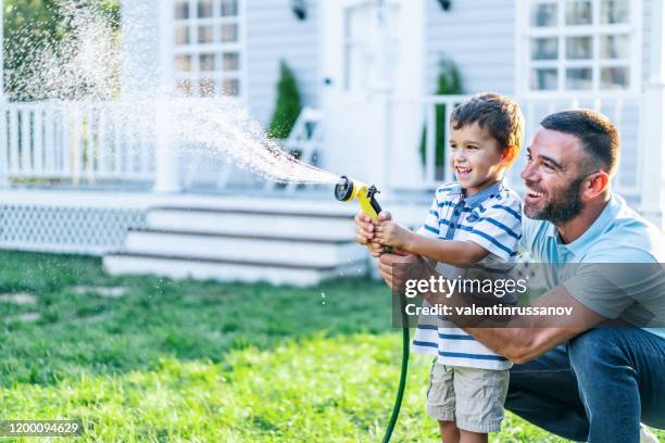 father splashing water and having fun with son on back yard - garden house stock pictures, royalty-free photos & images