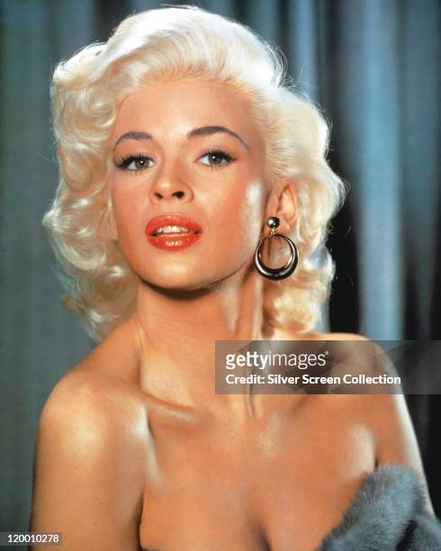 Headshot of Jayne Mansfield , US actress, wearing circular earrings in a studio portrait, against a bluebackground, circa 1955.