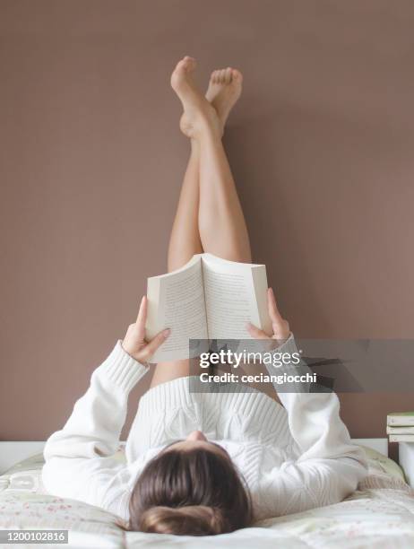 teenage girl lying on her bed reading a book - barefoot feet up lying down girl stockfoto's en -beelden