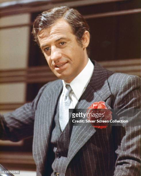 Jean-Paul Belmondo, French actor, swearing a dark blue pinstripe suit, with matching wasitcoat, a white shirt and a light grey tie, with a red flower...