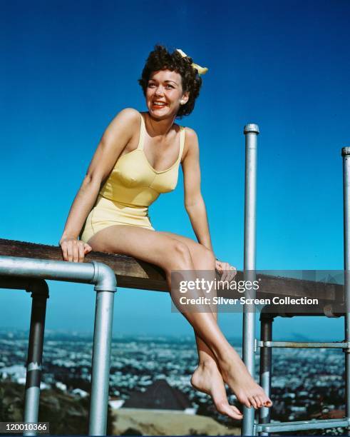 Jane Wyman , US actress, wearing a yellow swimsuit while sitting on a diving board, with a background of blue sky, circa 1950.